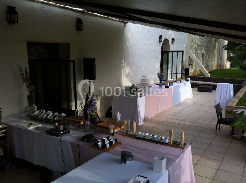 Tables dressées pour un buffet en extérieur sous un auvent, avec nappes blanches et décoration florale.