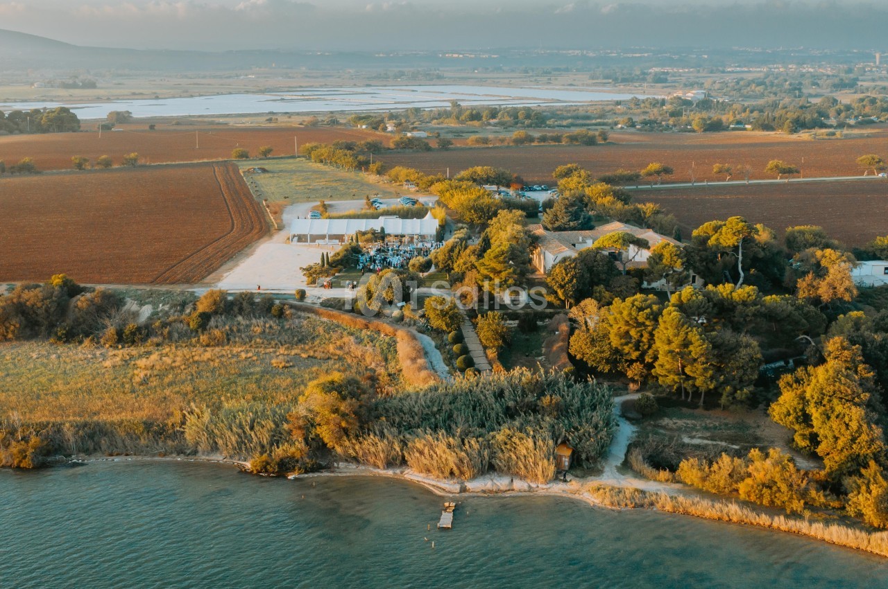Vue aérienne d'un domaine entouré de champs, de végétation et bordé par un plan d'eau avec un petit ponton.