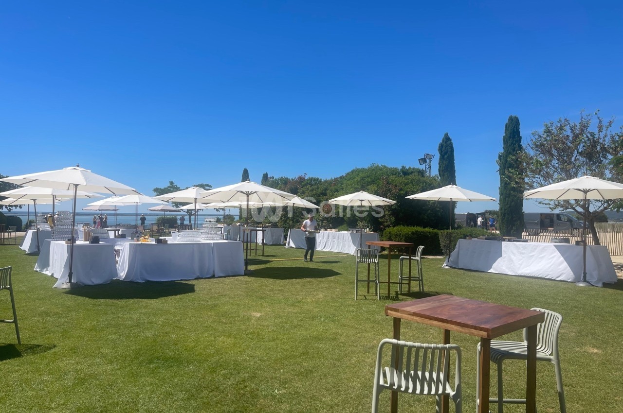Tables et parasols blancs disposés sur une pelouse en plein air par une journée ensoleillée.