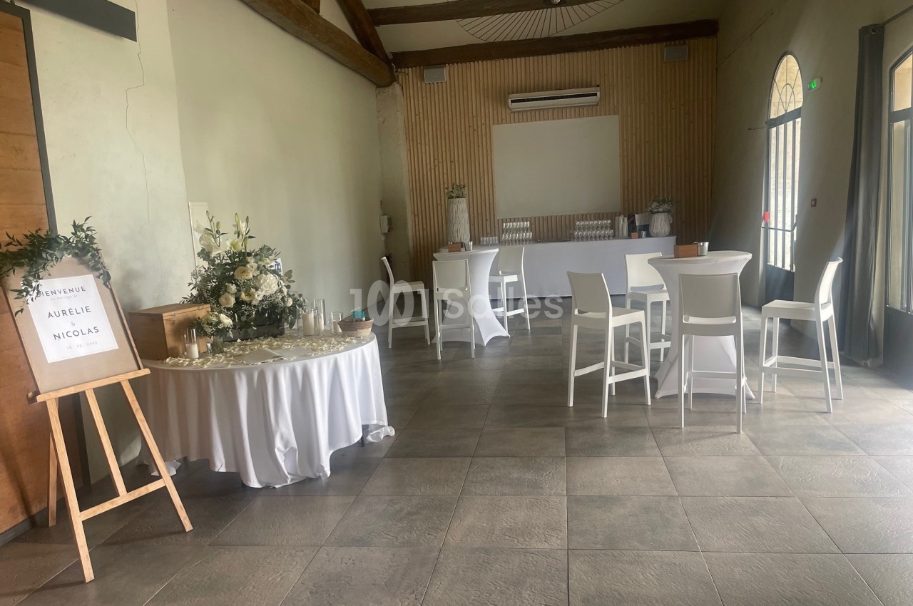 Salle de réception lumineuse avec tables décorées, panneau de bienvenue et espace bar en arrière-plan.