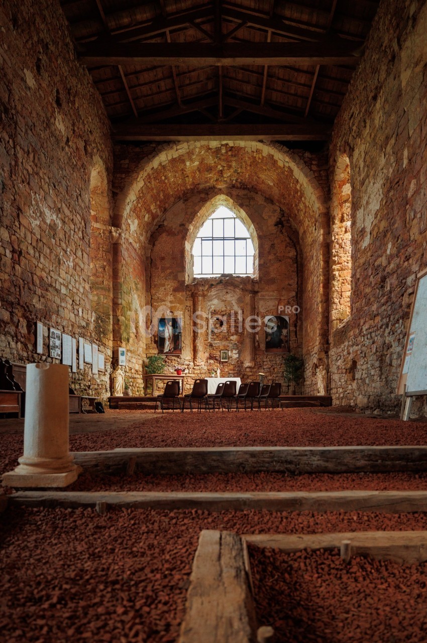 Intérieur d'une église en pierre ancienne avec des chaises alignées, un autel et une grande fenêtre gothique.