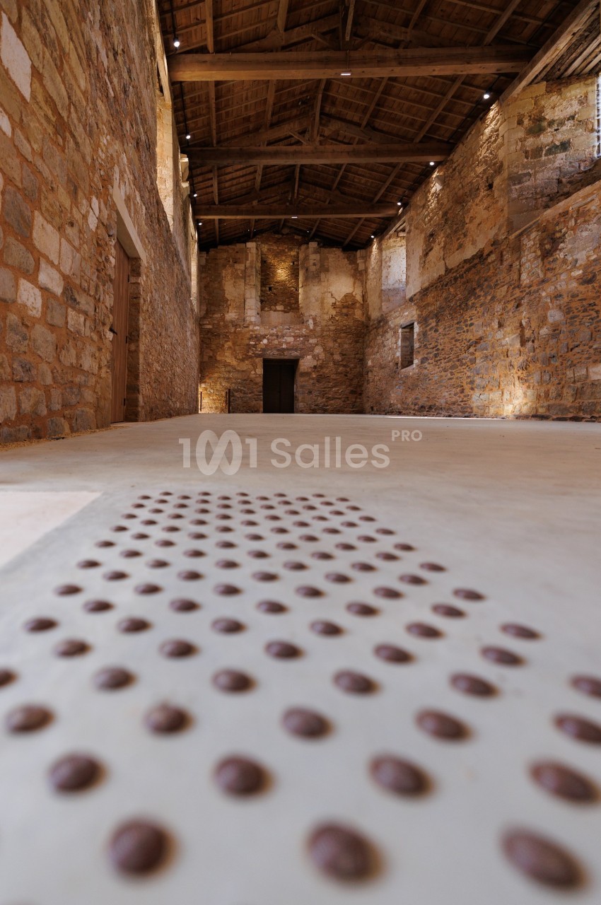 Intérieur d'un bâtiment en pierre avec un sol tactile pour guider les personnes malvoyantes vers une porte au fond.