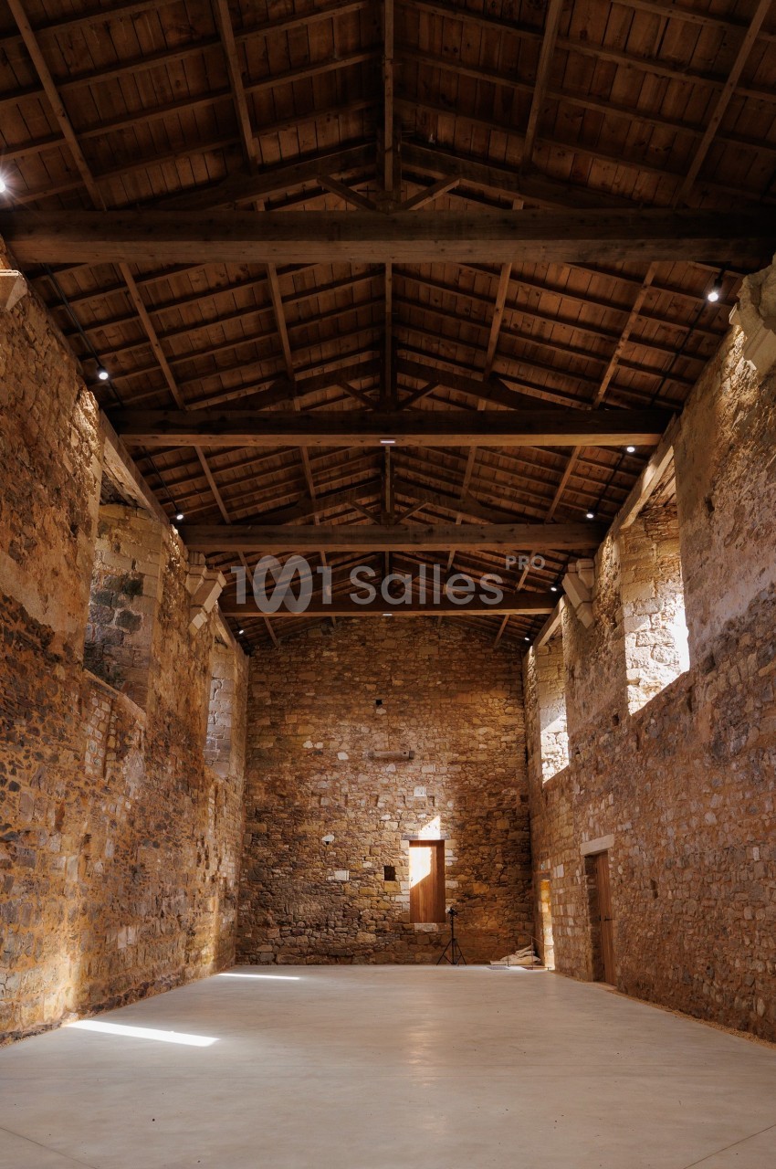 Intérieur d'un bâtiment en pierre avec un plafond en bois, éclairé par des ouvertures laissant entrer la lumière naturelle.
