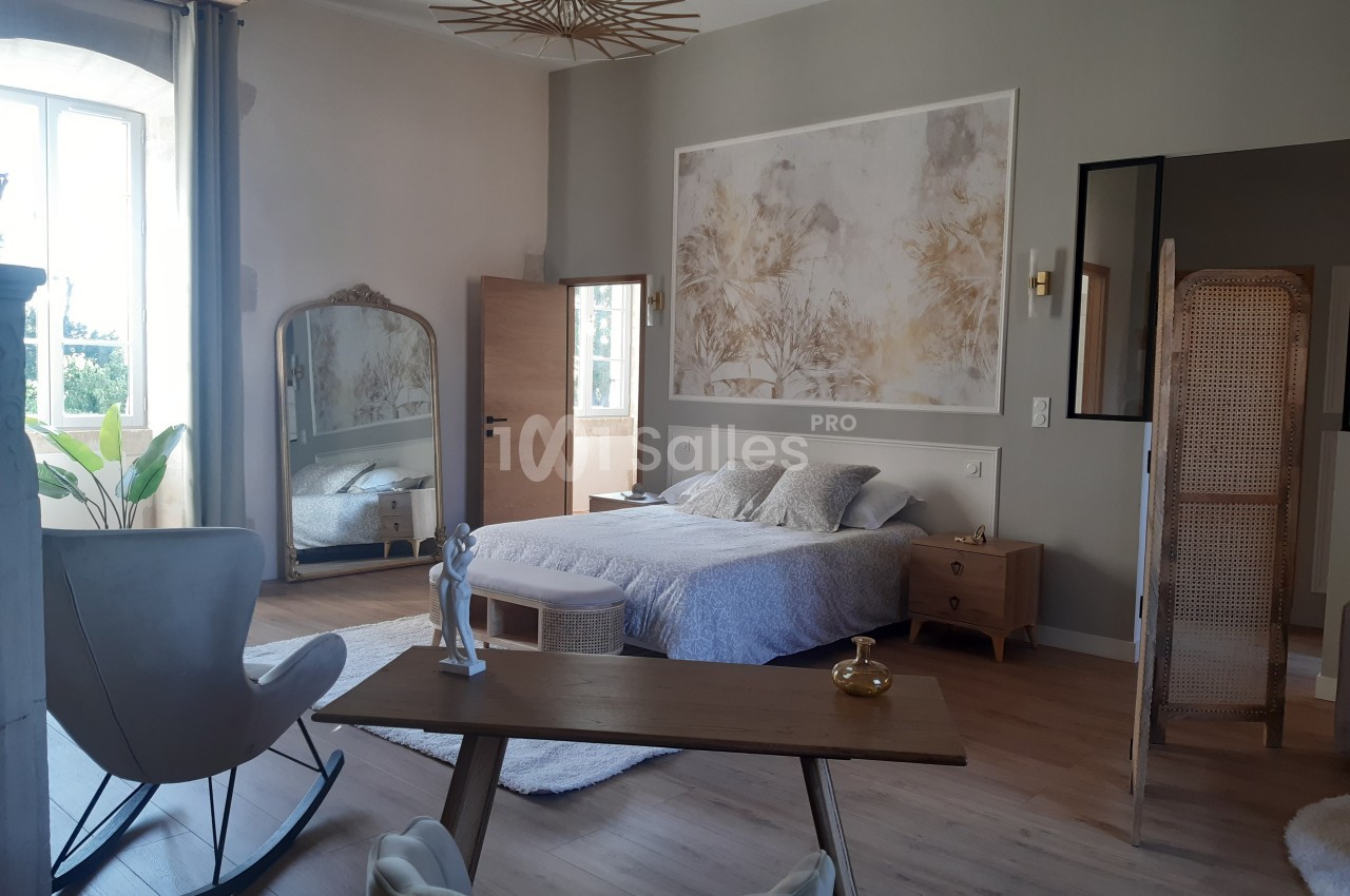 Chambre lumineuse avec lit double, bureau en bois, miroir sur pied, paravent en rotin et décoration murale.