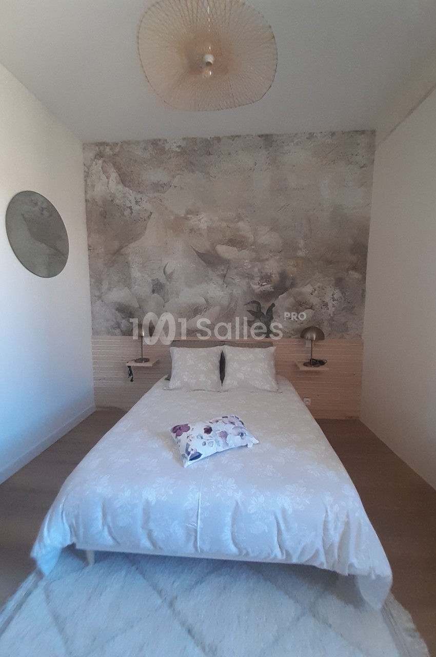 Chambre avec un lit double, tête de lit en bois clair, mur décoré d'une fresque florale et éclairage mural discret.