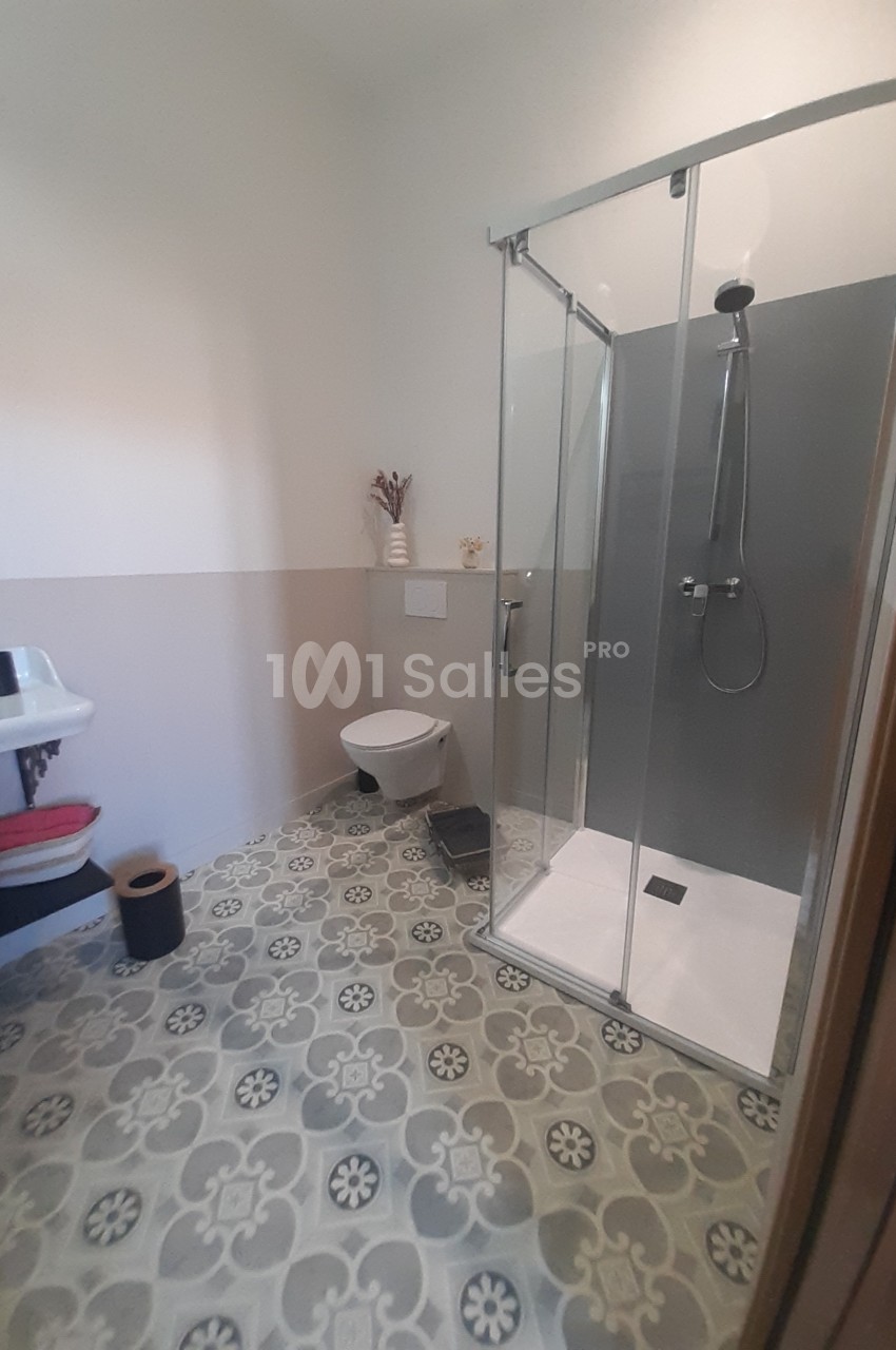 Salle de bain avec douche vitrée, lavabo, toilettes suspendues et sol en carreaux à motifs géométriques.