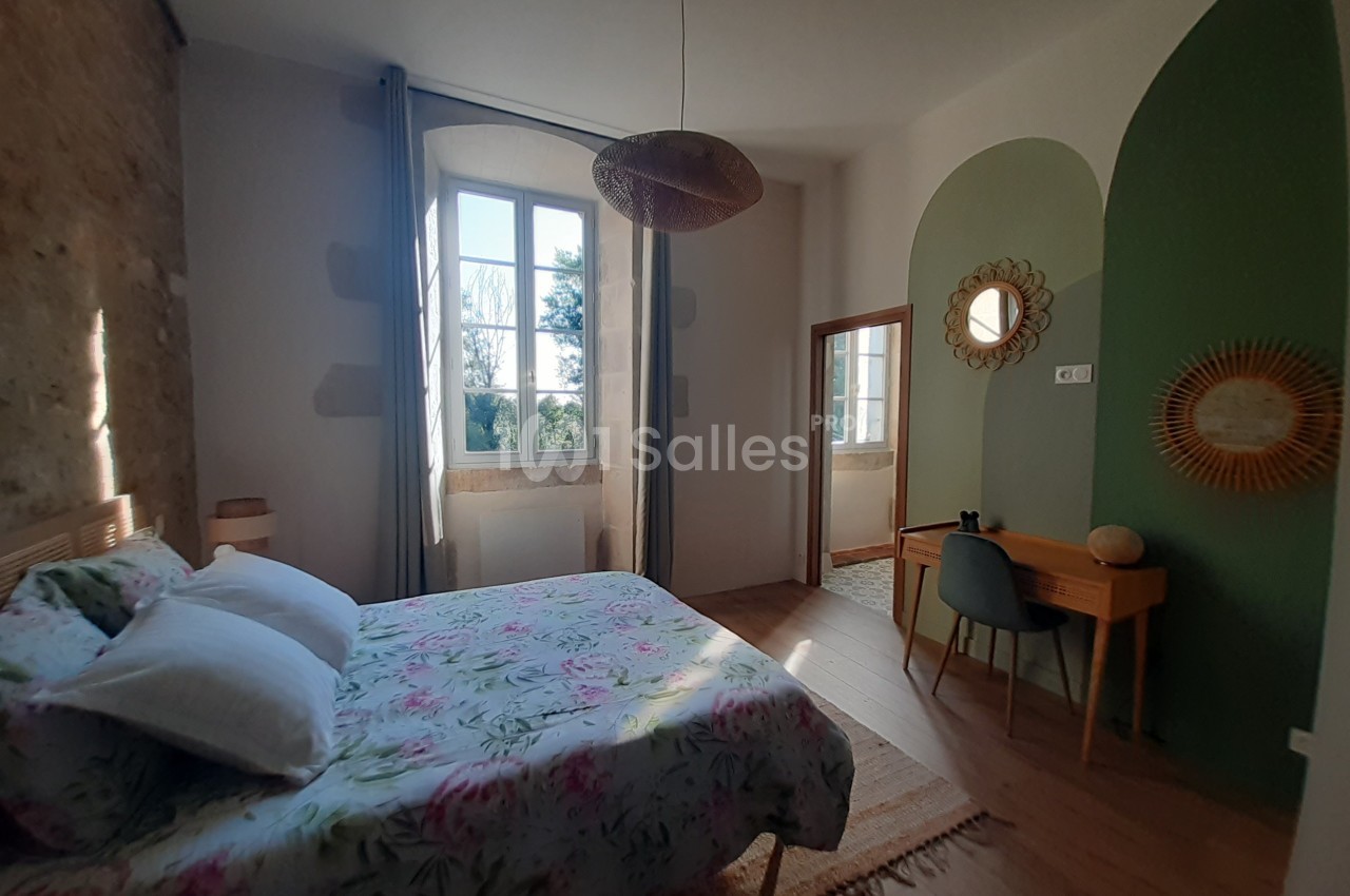 Chambre lumineuse avec lit double, bureau en bois, miroir rond et mur partiellement peint en vert.