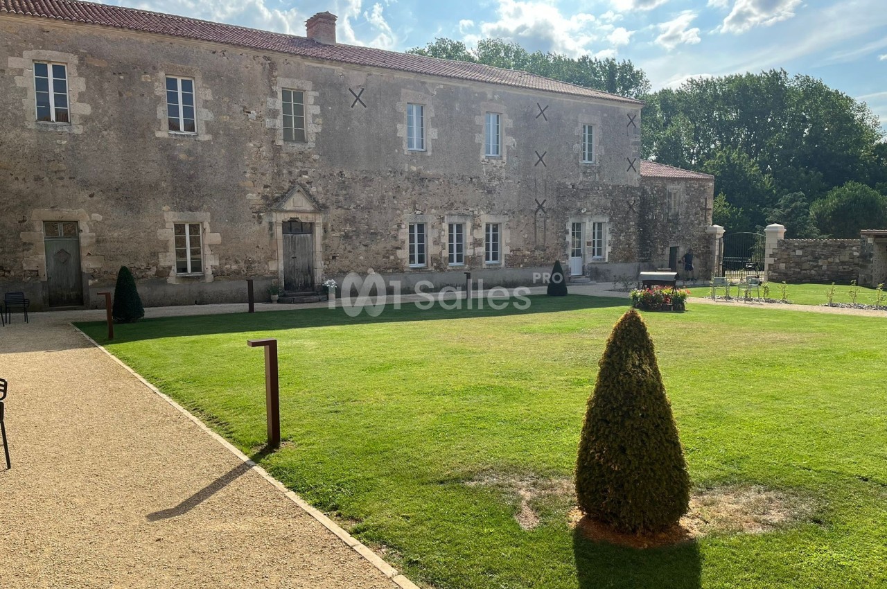 Façade d'un bâtiment en pierre entouré d'une pelouse bien entretenue et d'allées gravillonnées, sous un ciel partiellement…