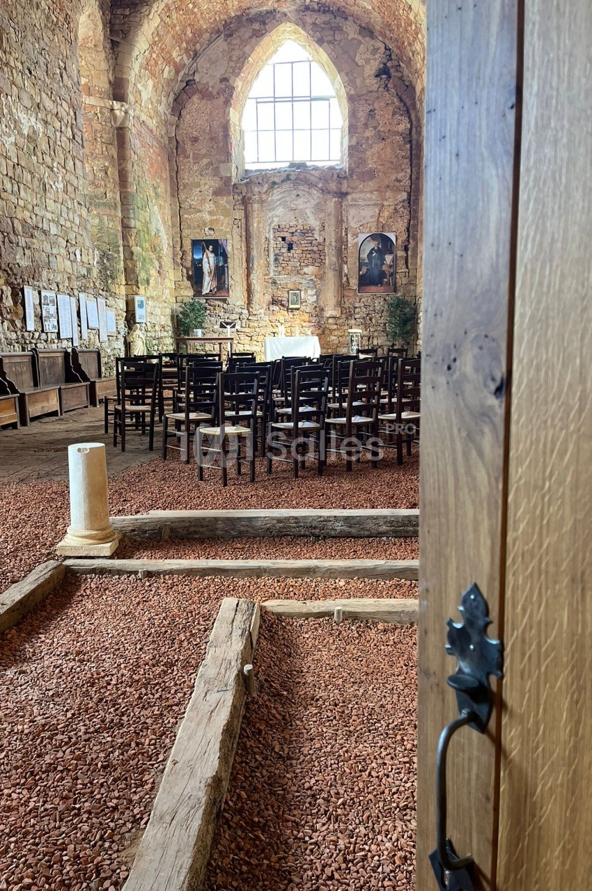 Intérieur d'une chapelle en pierre avec des rangées de chaises, un autel au fond et une porte en bois entrouverte au premier…