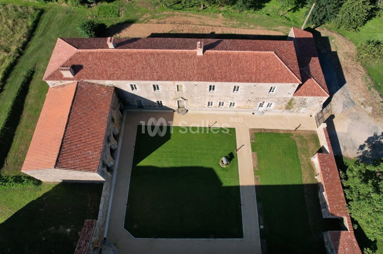 Vue aérienne d'un bâtiment historique en pierre avec toit en tuiles rouges entourant une cour centrale gazonnée.