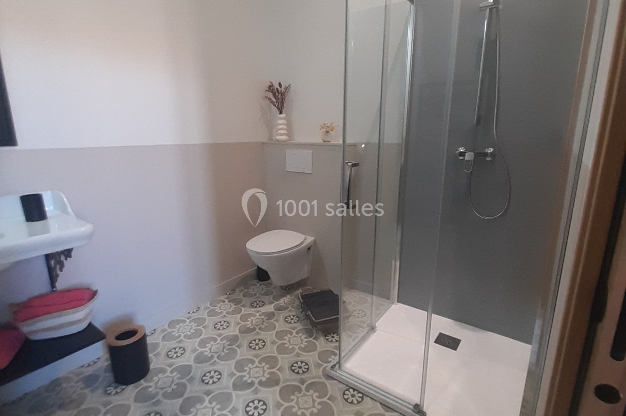 Salle de bain avec douche vitrée, lavabo, toilettes suspendues et sol en carreaux de ciment décoratifs.