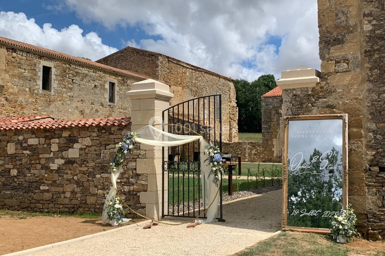 Entrée d'un domaine en pierre avec une arche décorée de fleurs et un panneau indiquant un événement.