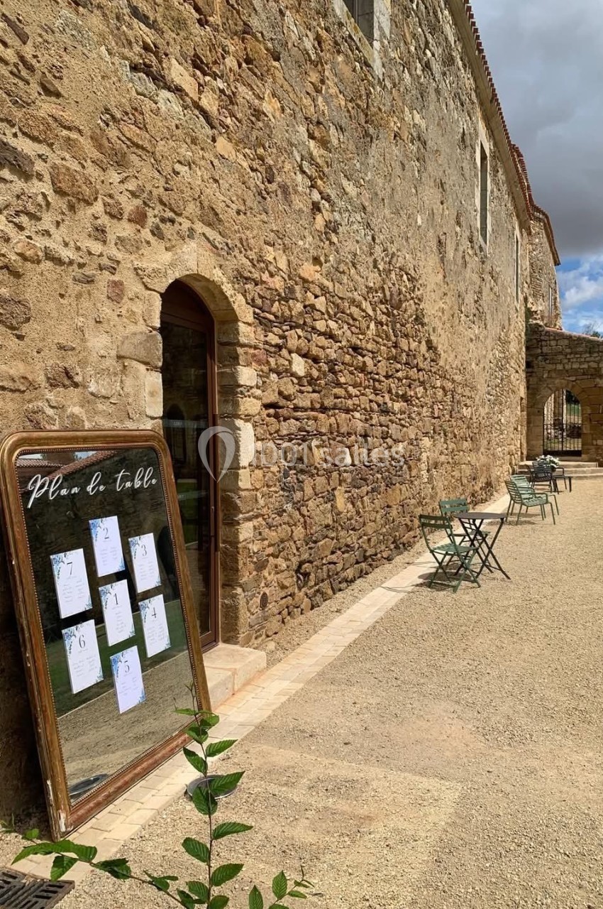 Panneau avec un plan de table posé contre un mur en pierre, entouré de chaises et tables extérieures.