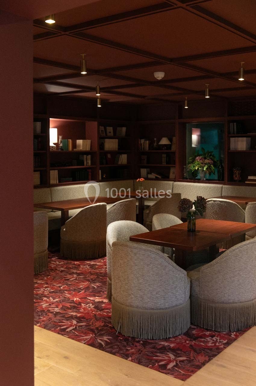 Espace de lecture avec tables en bois, fauteuils à franges et étagères remplies de livres, éclairage tamisé.
