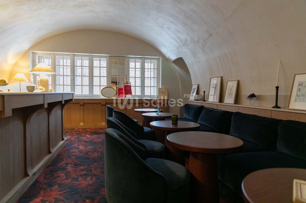 Salle voûtée avec canapés en velours, tables en bois, éclairage doux et fenêtres laissant entrer la lumière naturelle.