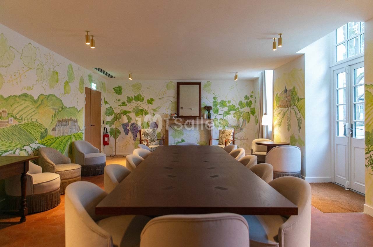 Salle de réunion lumineuse avec une grande table en bois, des fauteuils clairs et des murs décorés de fresques végétales.