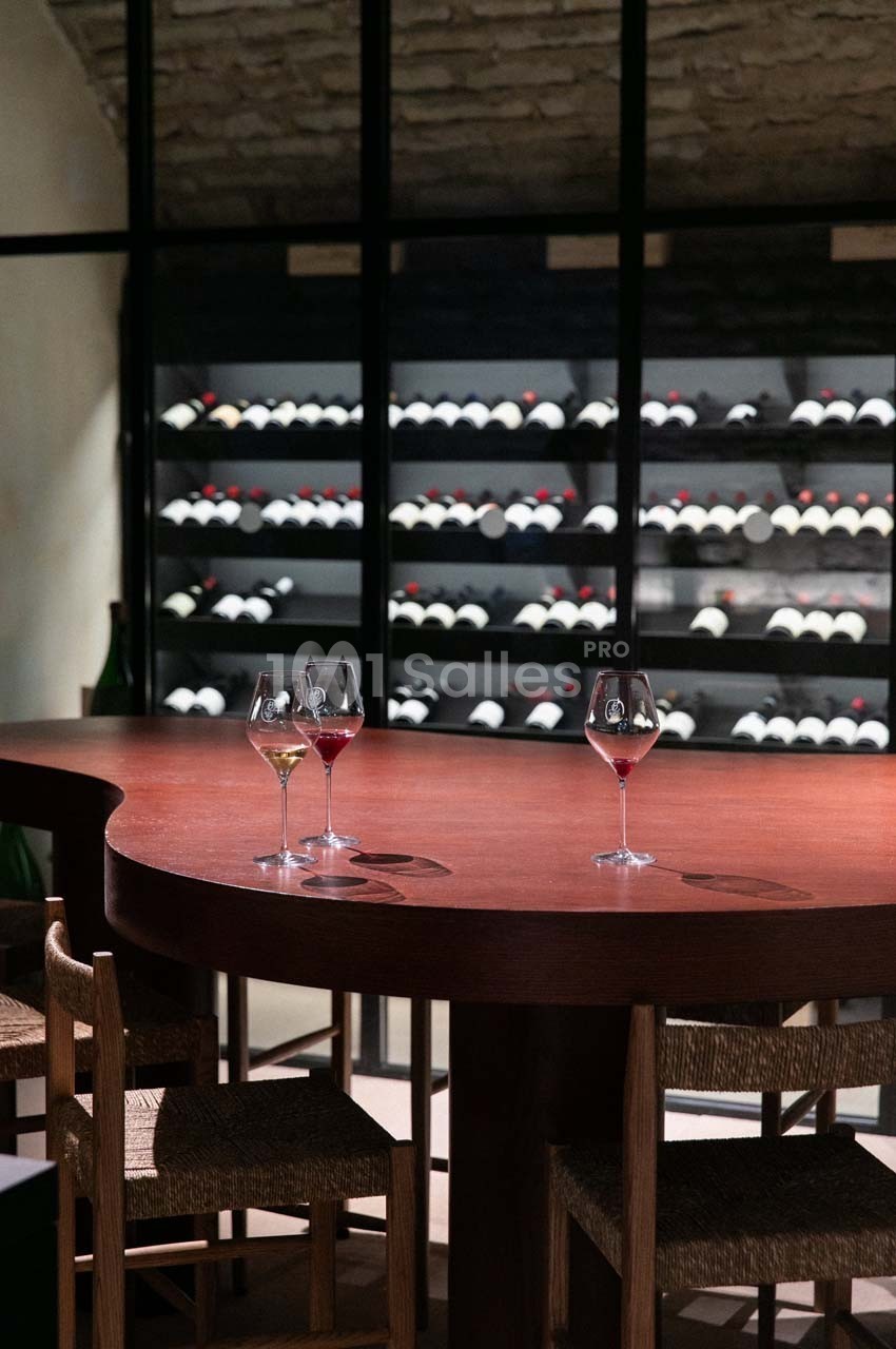 Salle de dégustation avec table en bois, verres de vin et étagères remplies de bouteilles en arrière-plan.