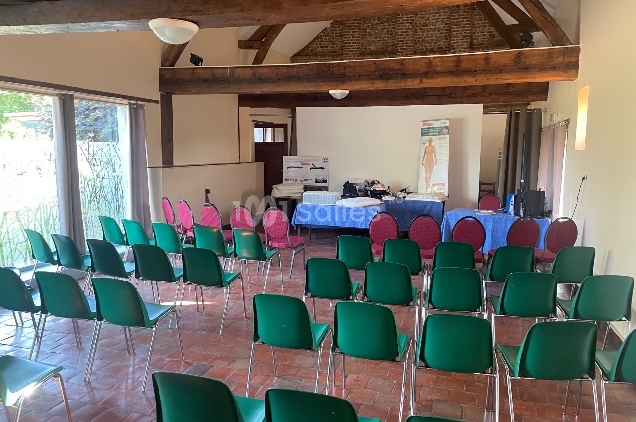 Salle de conférence avec des chaises vertes alignées face à une table recouverte de nappes bleues, sous une charpente en…
