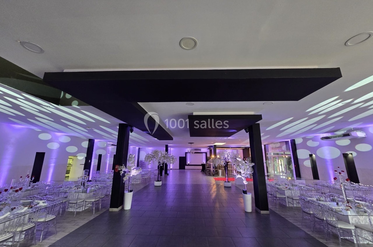 Salle de réception moderne avec éclairage violet, tables décorées et chaises transparentes alignées.