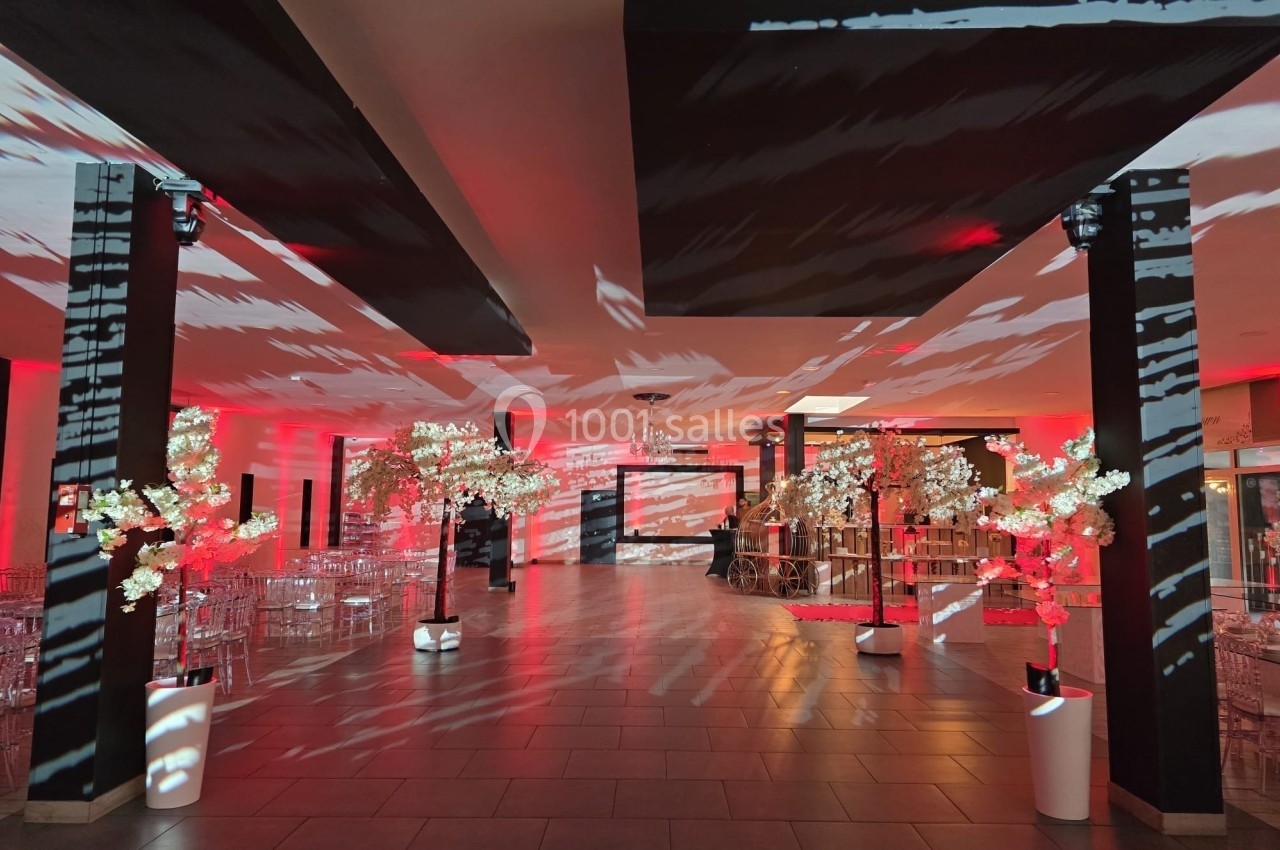 Salle de réception décorée avec des lumières rouges, des colonnes noires et des arbres lumineux blancs.