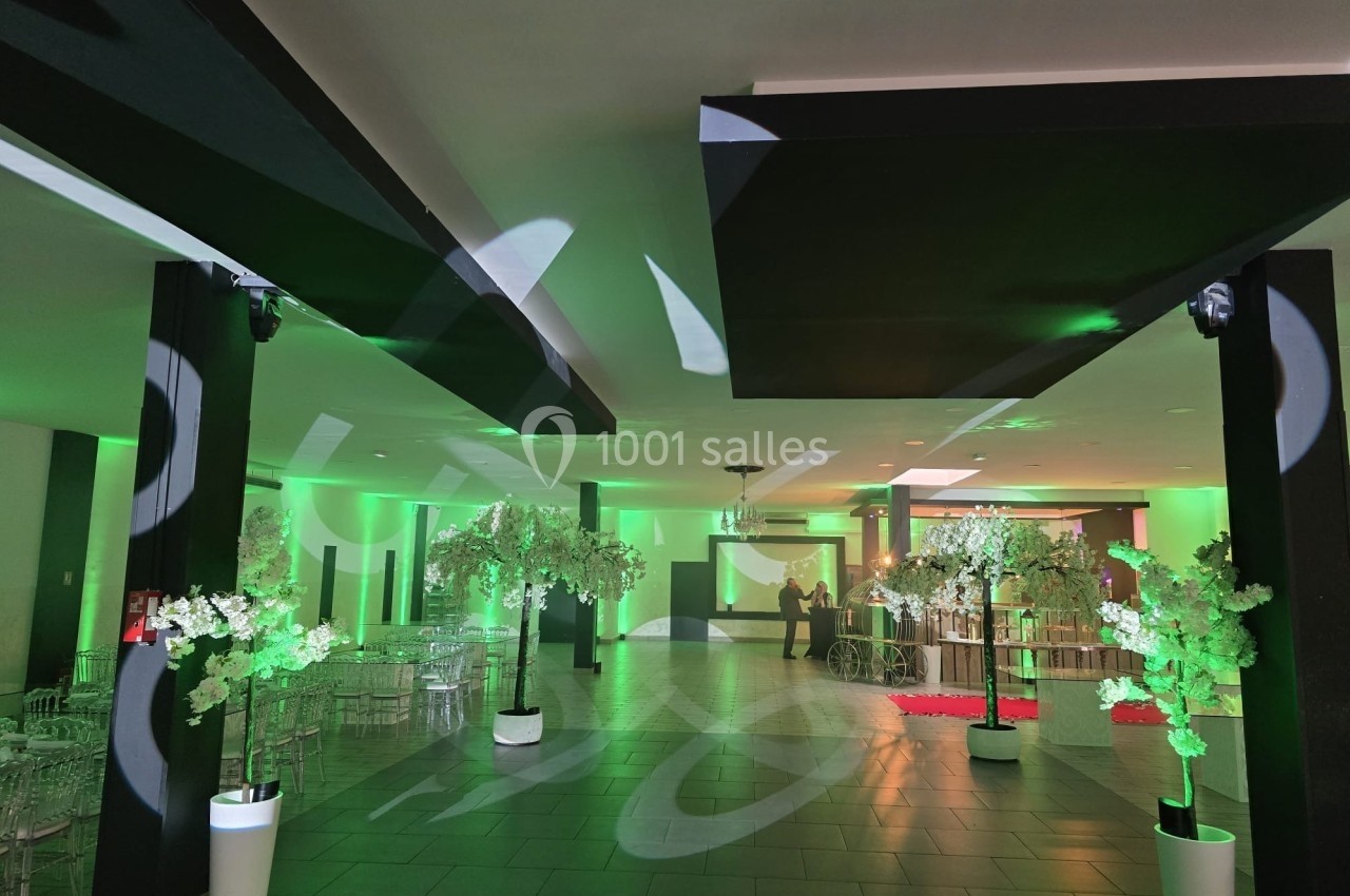 Salle de réception décorée avec des arbres artificiels et éclairages verts, tables et chaises disposées en arrière-plan.
