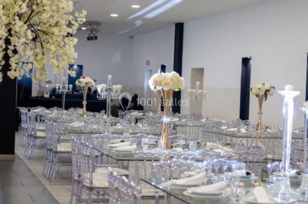 Salle de réception décorée avec des tables en verre, chaises transparentes et arrangements floraux blancs.