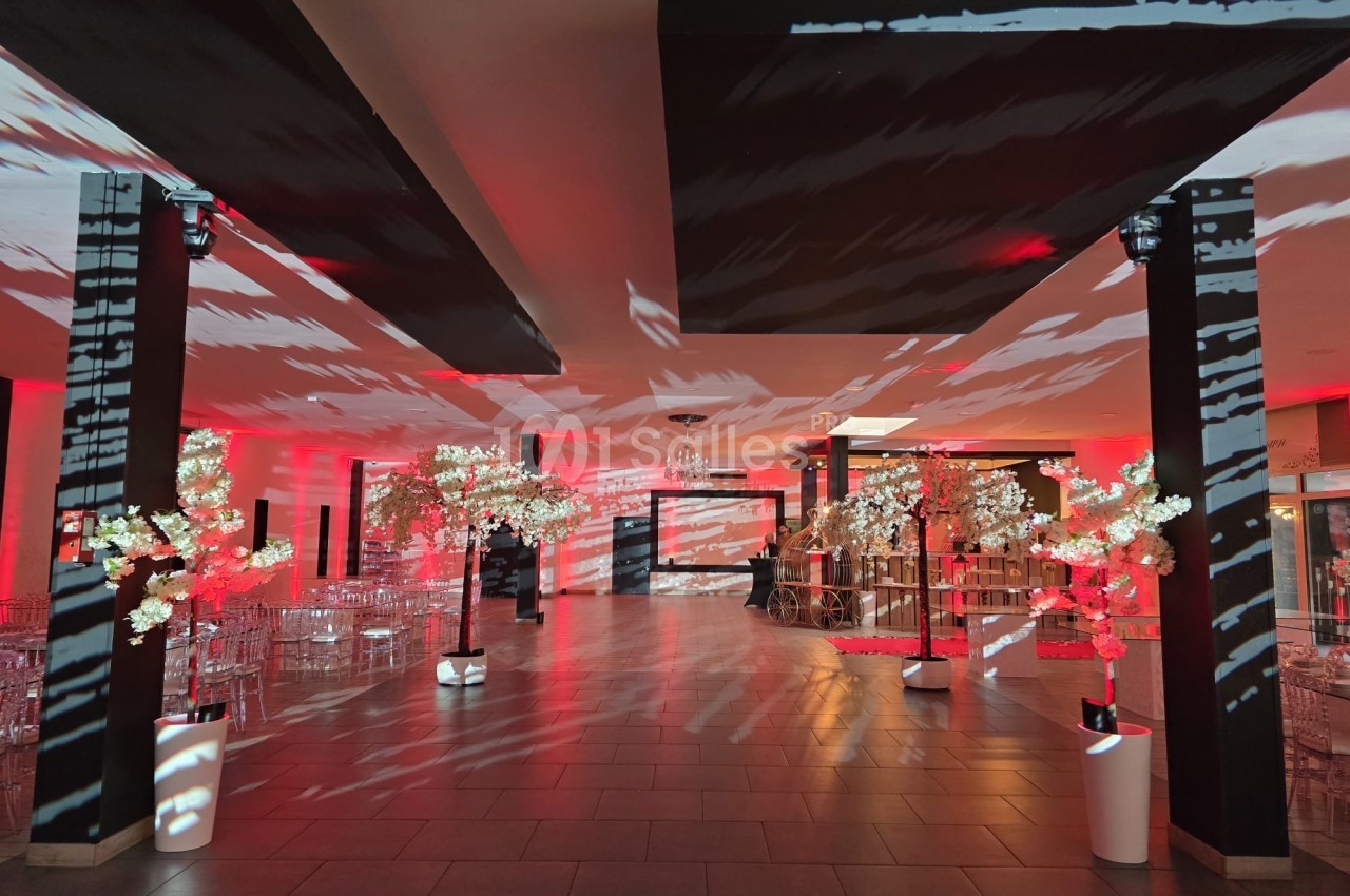 Salle de réception décorée avec des lumières rouges, des colonnes noires et des arbres lumineux blancs.