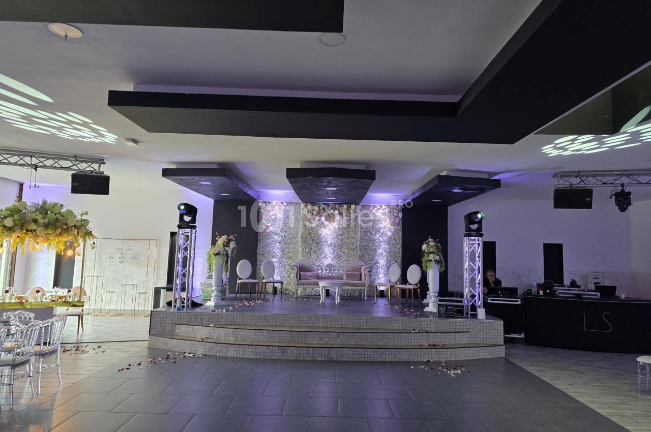 Salle de réception décorée avec une scène centrale, éclairage tamisé et arrangements floraux élégants.