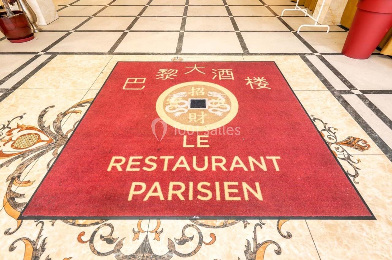 Tapis rouge avec inscriptions en français et en chinois, placé sur un sol carrelé à l'entrée d'un établissement.