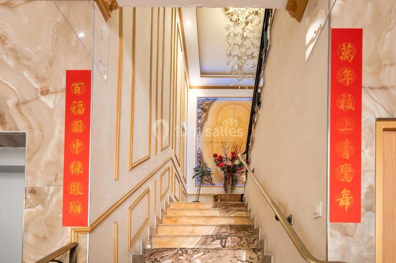 Escalier intérieur décoré de panneaux rouges avec des caractères chinois dorés et un grand tableau floral au mur.