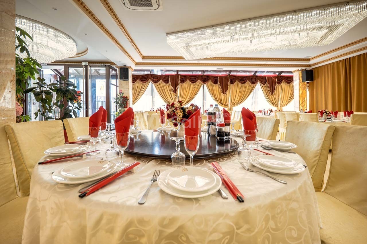 Table dressée avec nappes blanches, serviettes rouges, vaisselle élégante et centre de table floral dans une salle lumineuse.