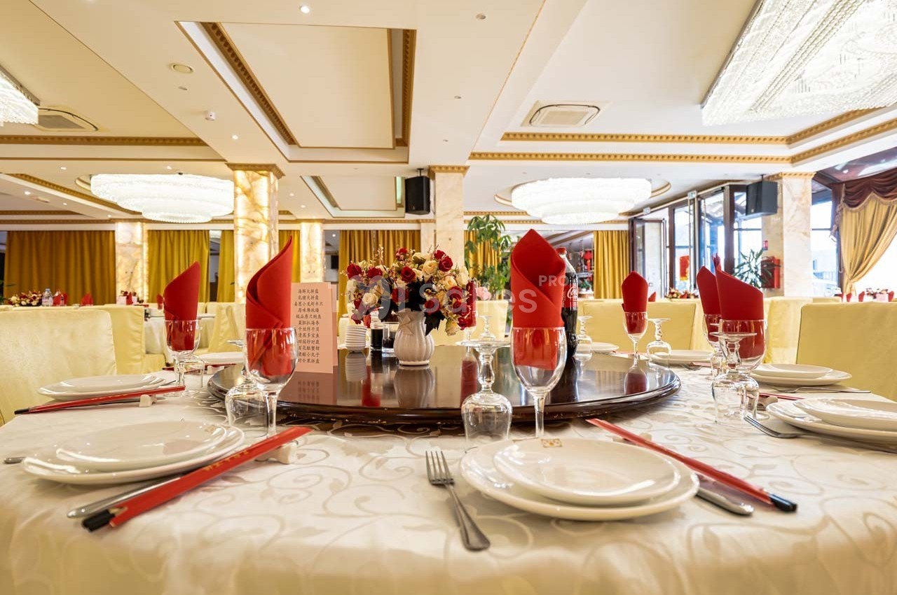 Table élégamment dressée avec nappes blanches, serviettes rouges pliées, vaisselle et centre de table floral dans une salle…