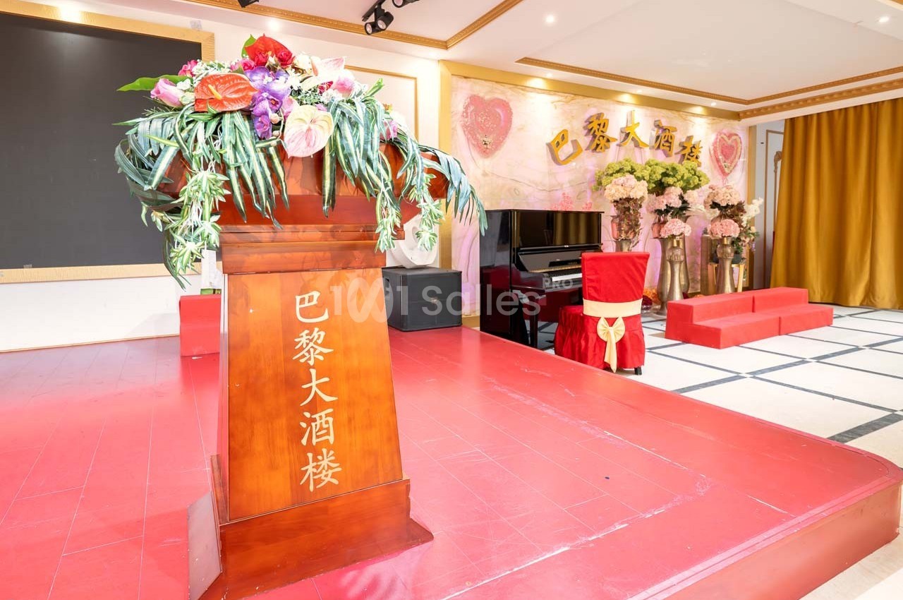 Un pupitre en bois orné de fleurs devant une scène décorée de rideaux dorés et de panneaux roses.