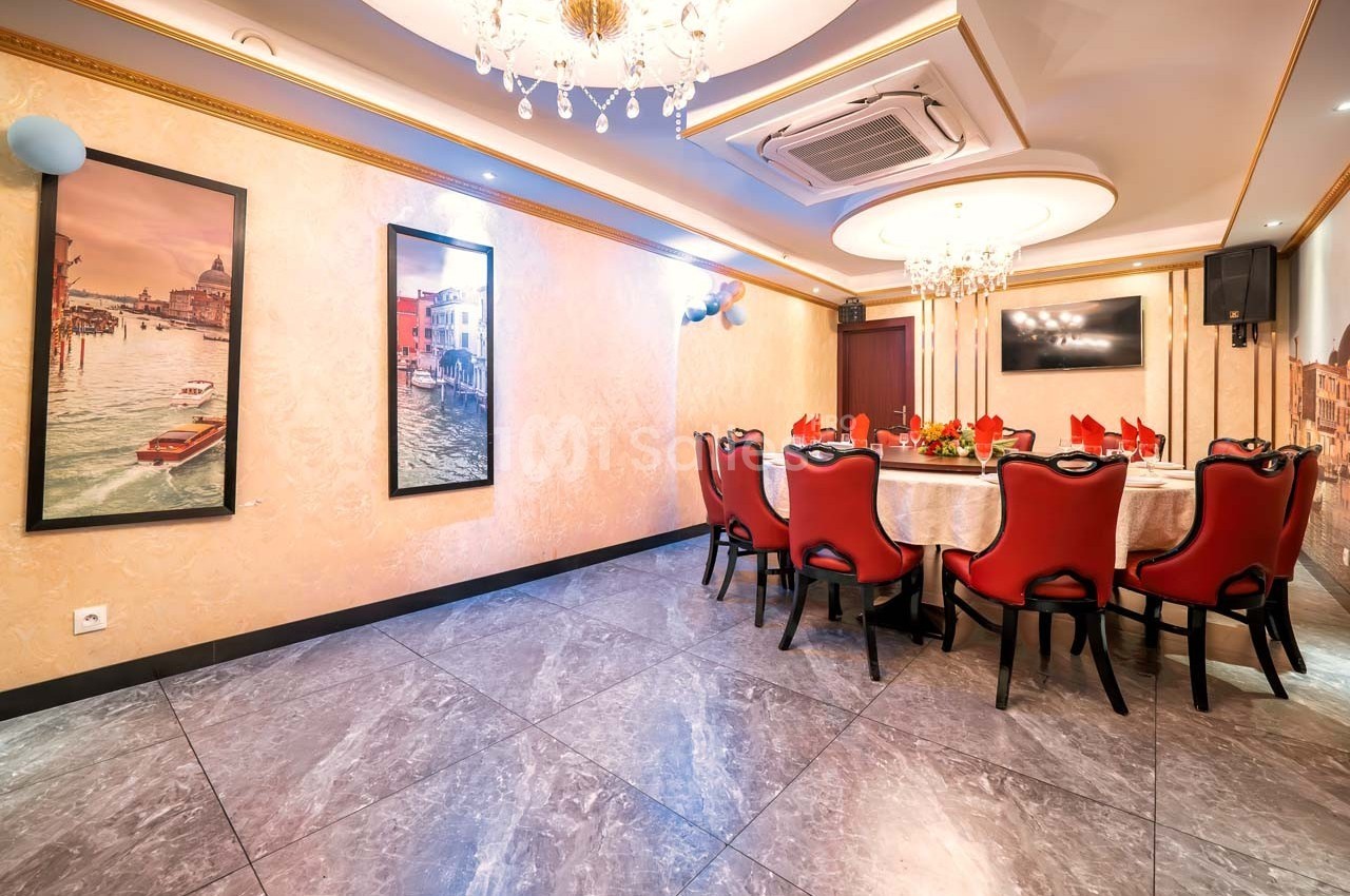 Salle à manger élégante avec table dressée, chaises rouges, lustres et décorations murales représentant des paysages urbains.