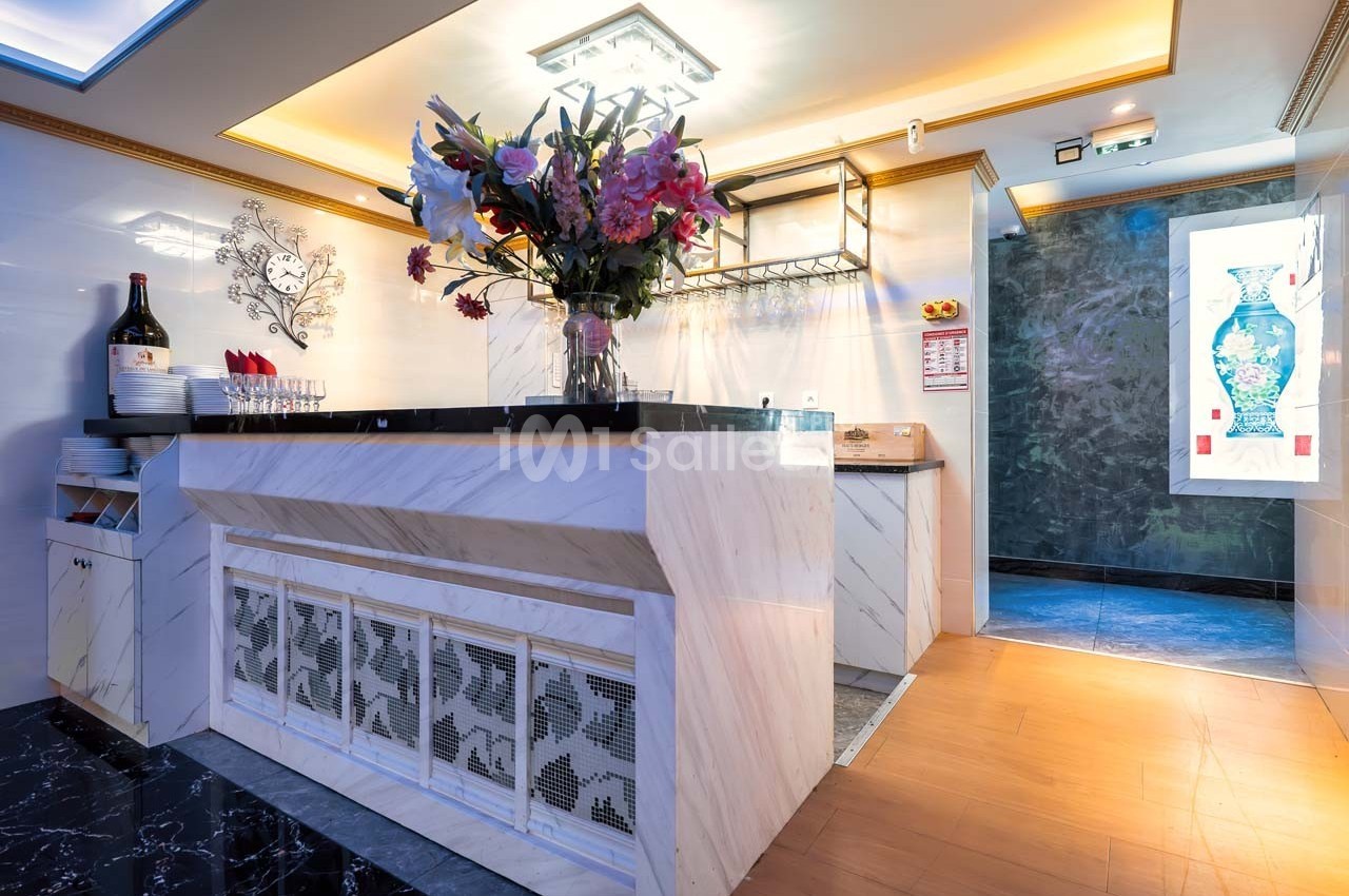 Comptoir en marbre blanc décoré d'un grand vase de fleurs, avec des étagères et un mur éclairé en arrière-plan.