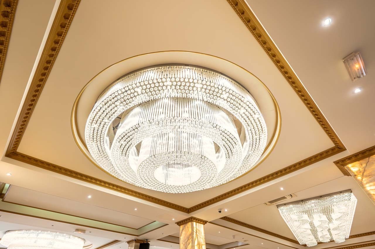 Plafond orné d'un grand lustre en cristal lumineux, entouré de moulures dorées et de spots encastrés.