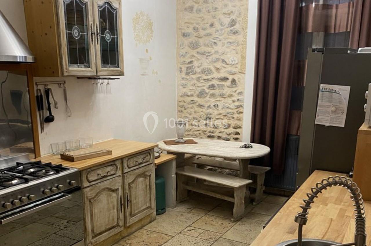 Cuisine rustique avec murs en pierre, table en bois, gazinière, évier moderne et meubles en bois vieilli.