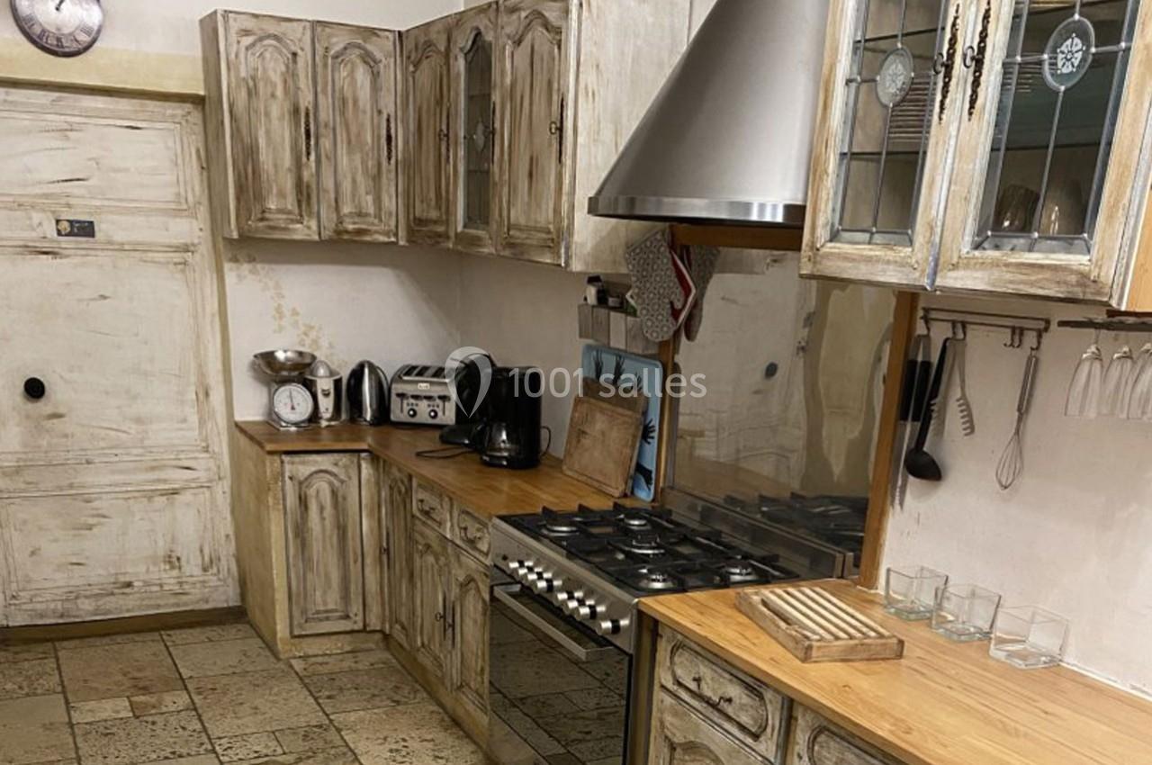 Cuisine rustique avec meubles en bois vieilli, plan de travail en bois, électroménagers modernes et sol en pierre.