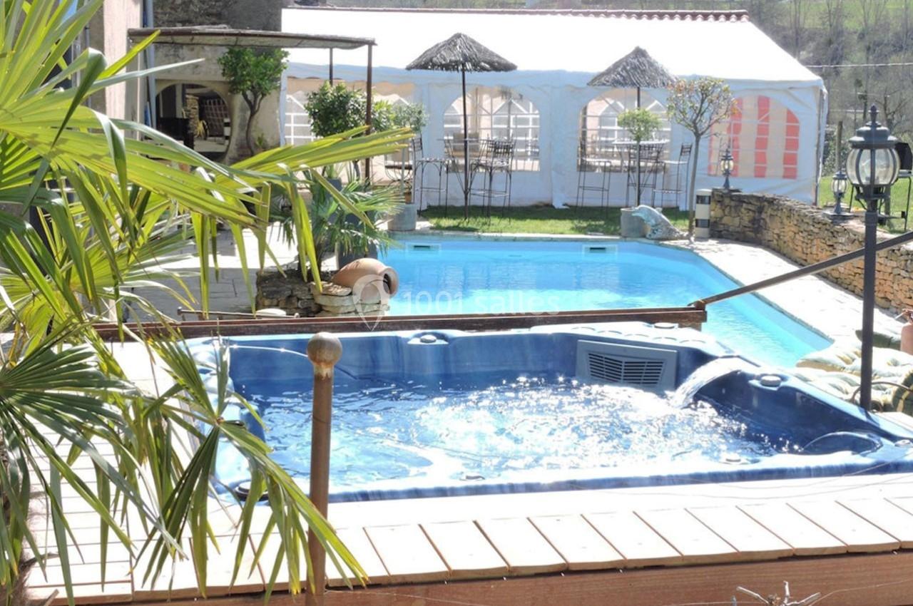 Vue d'une terrasse avec jacuzzi, piscine et tente aménagée dans un jardin ensoleillé.