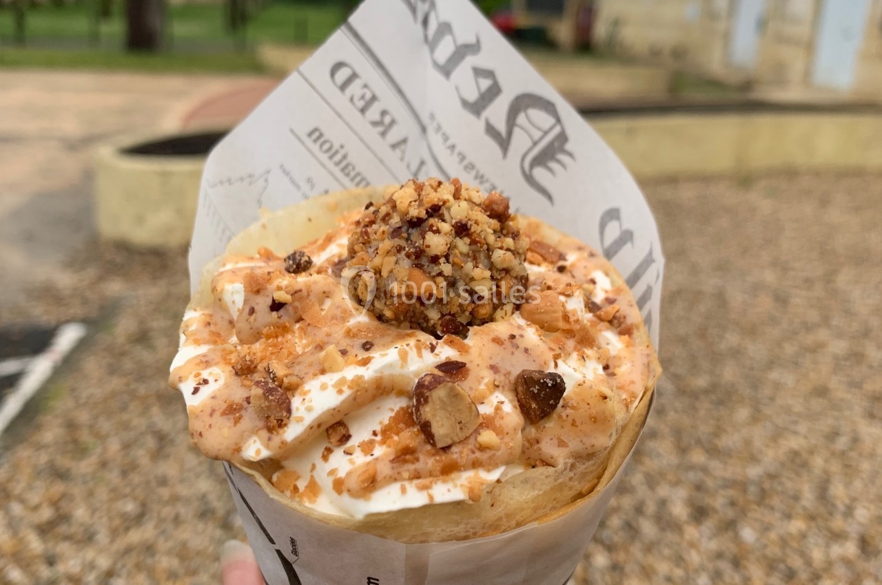 Glace en cornet garnie de crème, éclats de noisettes et caramel, tenue à la main dans un parc.