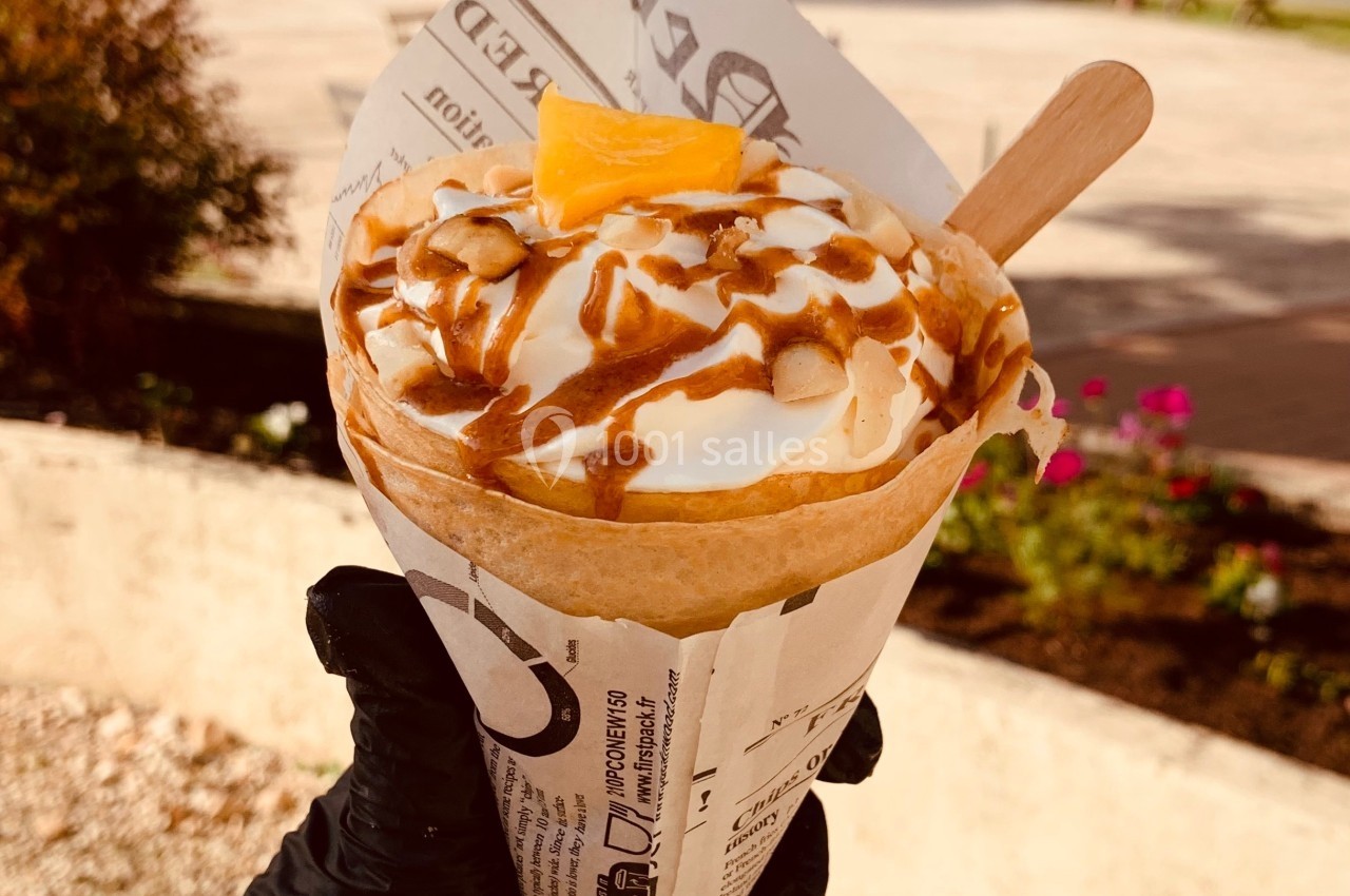 Crêpe roulée garnie de chantilly, caramel et amandes, tenue à la main dans un parc ensoleillé.