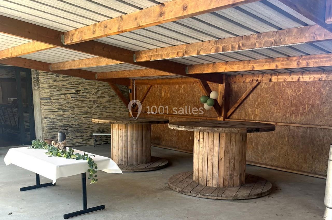 Abri en bois avec deux tables rondes en bois recyclé, une table rectangulaire décorée et un mur en pierre apparente.