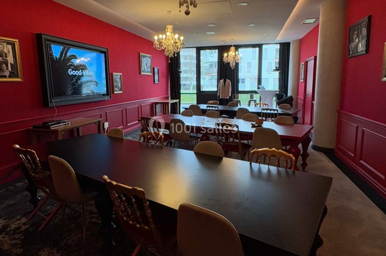 Salle de réunion lumineuse avec murs rouges, tables noires, chaises variées et écran affichant ’Good Vibes’.