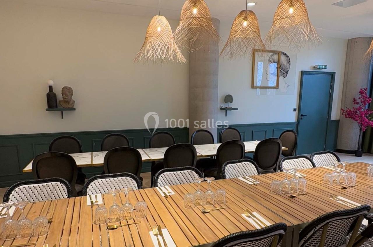 Salle à manger avec deux grandes tables en bois, chaises noires et luminaires suspendus en osier.