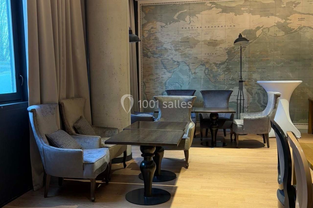 Salle avec des tables en bois, fauteuils gris et une grande carte murale en arrière-plan.