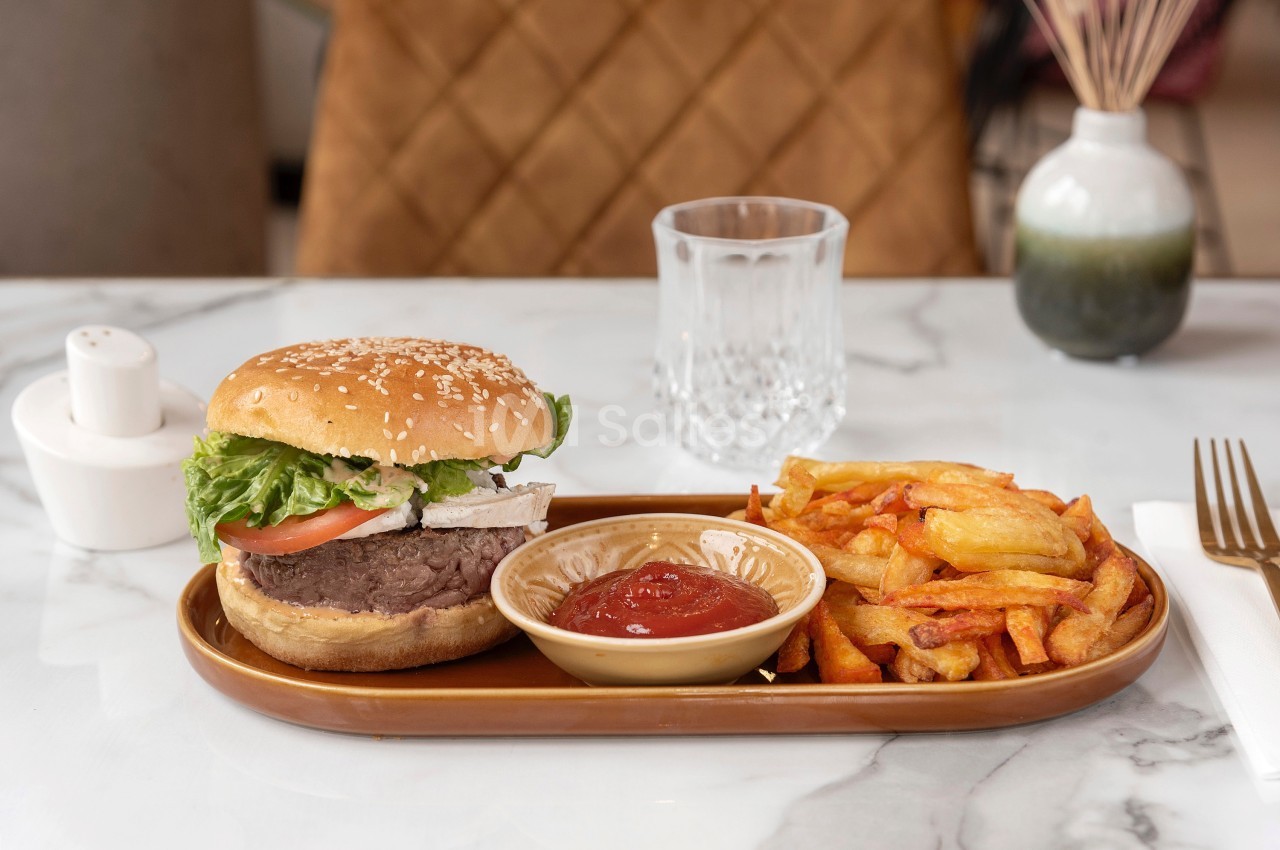 Assiette avec un burger garni de légumes, des frites dorées et une coupelle de ketchup, sur une table en marbre.