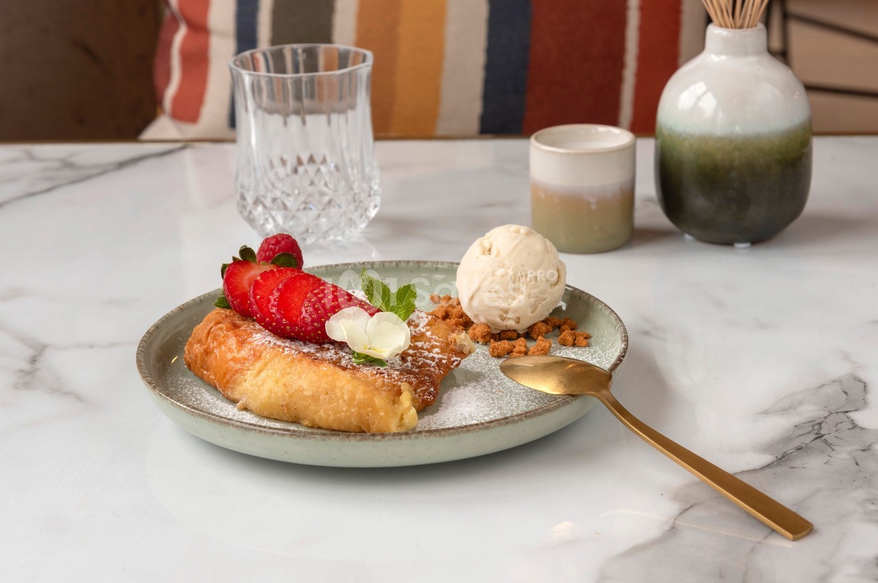Assiette avec une pâtisserie garnie de fraises, crème glacée, miettes croustillantes et sucre glace, sur une table en marbre.