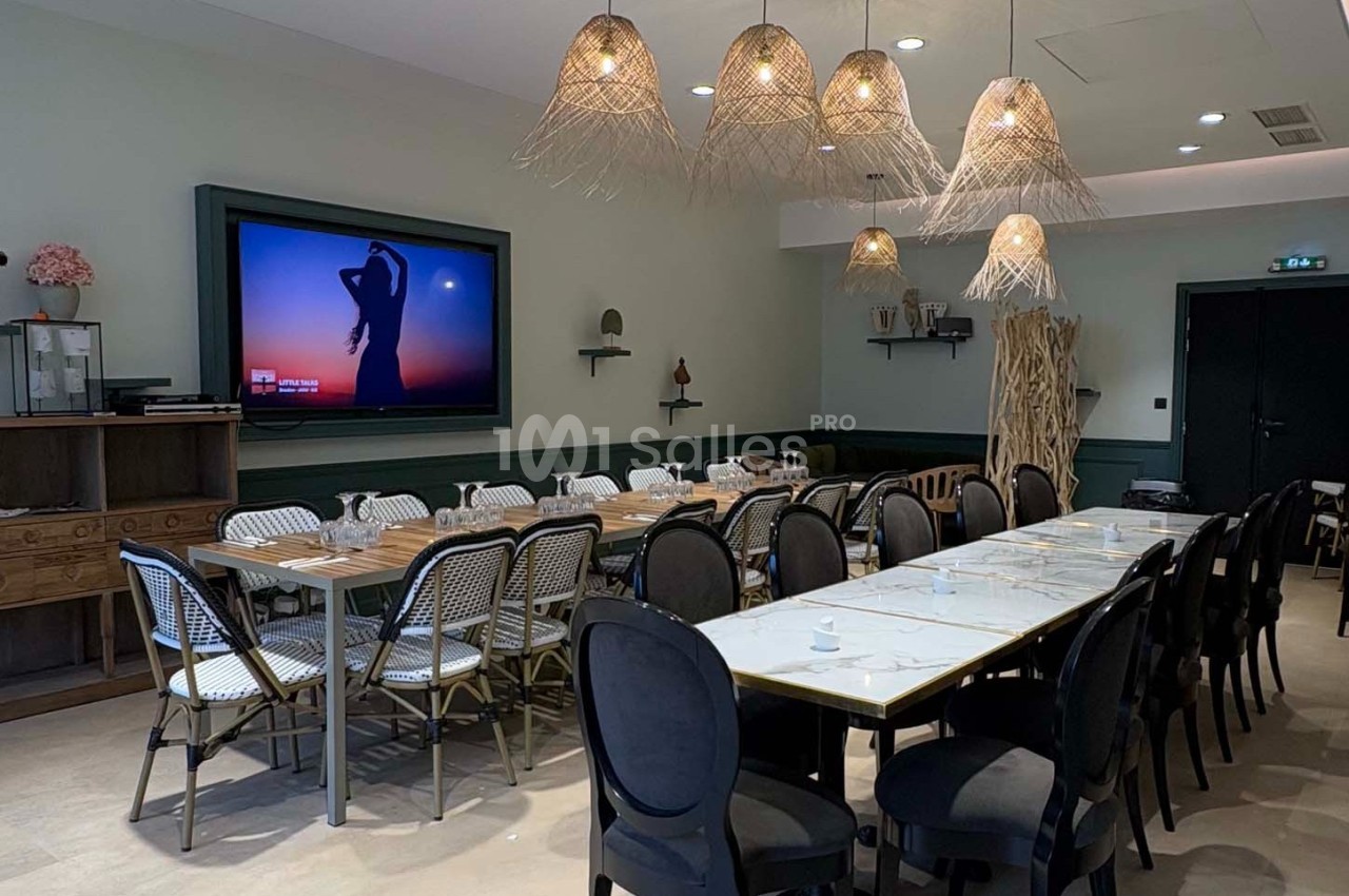 Salle de réunion lumineuse avec tables alignées, chaises variées, écran mural et suspensions en osier.