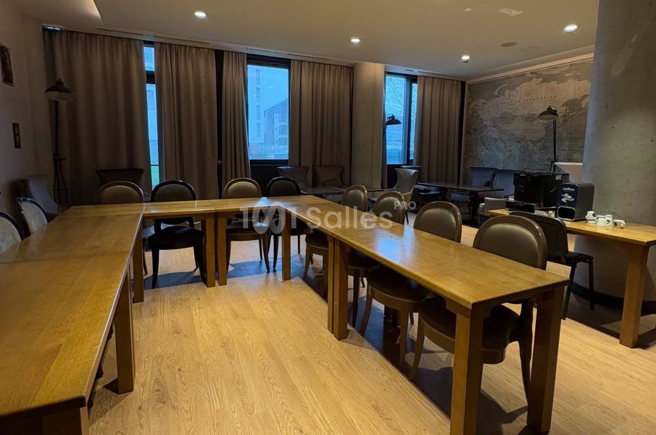 Salle de réunion avec tables en bois disposées en U, chaises assorties et grandes fenêtres avec rideaux.