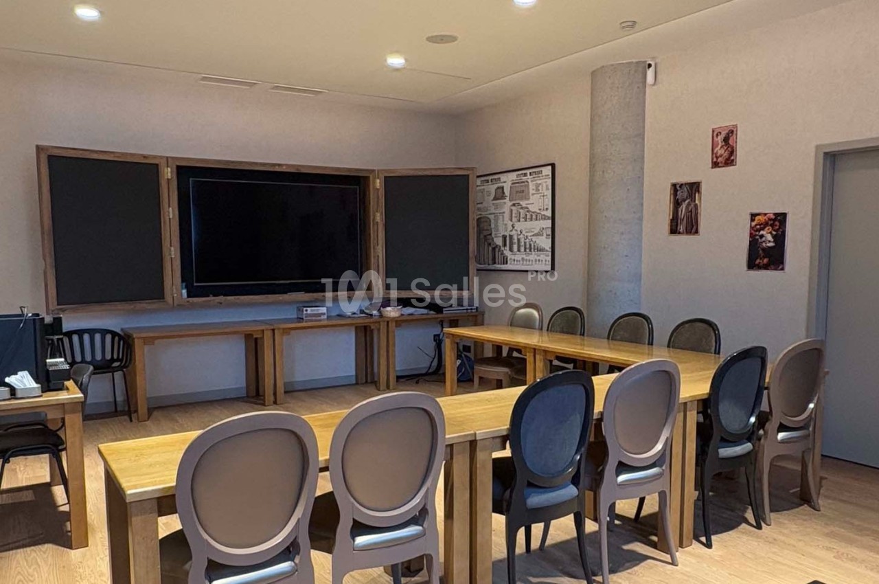 Salle de réunion avec tables en bois, chaises modernes, grand écran mural et décorations murales.